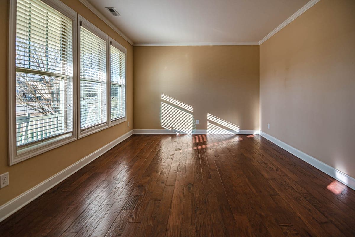 An empty rented apartment room with wooden flooring and a bright window