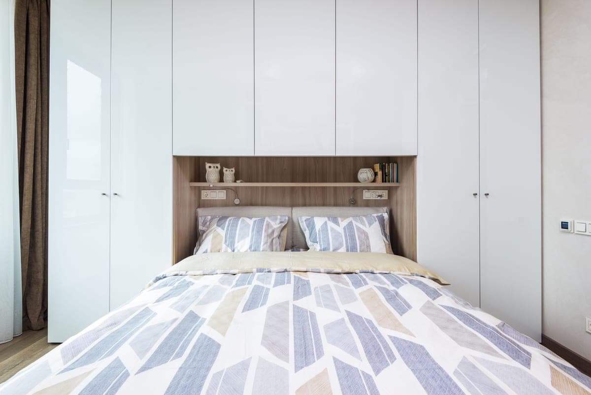 A bedroom wall fitted with tall white cabinetry and shelving beside the bed
